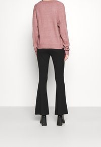 Rosa stickad tröja med avslappnad passform och ribbade manschetter, tillsammans med svarta utsvängda byxor. Outfiten har klackboots med blockformat heel.