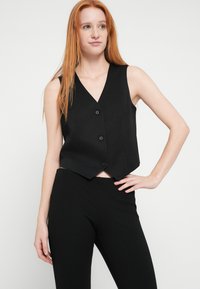 Mustast siidist varrukateta vest V-kaelusega, millel on kõverdatud alumine serv ja viis nööpi ees. Kandmisel mustad kõrge vöökohaga püksid.