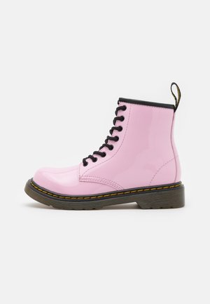 Skinnende pink snørestøvle til anklen med sorte snørebånd, sort øverste kant, gule syninger, tyk sort sål og træksløjfe bagpå.