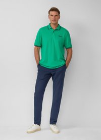 Zielona koszulka polo z czarnymi wykończeniami, w połączeniu z granatowymi spodniami i białymi trampkami. Koszulka polo ma klasyczny kołnierzyk i detal z logo.