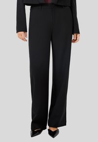 Pantalons large noirs en tissu lisse, avec une taille mi-haute, des passants de ceinture et un détail de couture discret le long des jambes.