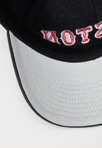 Black baseball cap with red embroidered text, gray undervisor, and structured crown. Features perforated detailing on the visor.