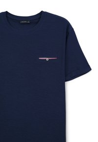 T-shirt in cotone blu navy con scollatura rotonda, maniche corte e piccola tasca sul petto con bottone e dettaglio a strisce rosse e bianche.
