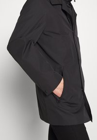 Czarna wodoodporna kurtka zapinana na zamek, z bocznymi kieszeniami i luźnym krojem. Posiada długie rękawy i minimalistyczny design.