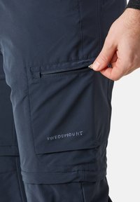Navy blue outdoor pants with a zippered pocket on the side, made from water-resistant fabric. Features "SWEDEMOUNT" logo in white embroidery.