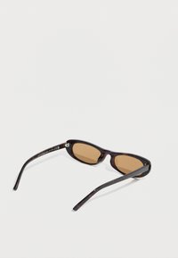 Καφέ γυαλιά ηλίου με σκελετό σε σκοτεινή χελώνα. Ο σχεδιασμός διαθέτει λεπτά, ίσια μπράτσα και στρογγυλούς φακούς.