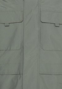 Grön, texturerad jacka med ett vertikalt ribbmönster, utrustad med två stora framfickor och en central dragkedja.