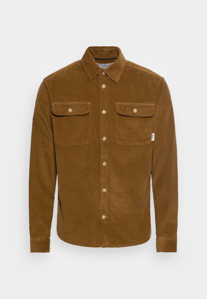 Chemise longue à manches en velours côtelé marron avec devant boutonné, col et deux poches poitrine boutonnées sur fond uni.