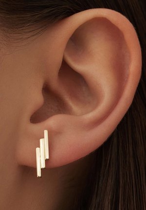 Gouden oorbellen met drie verticale metalen staven van verschillende lengtes, dicht bij het oorlel bevestigd, met een strakke, moderne uitstraling.