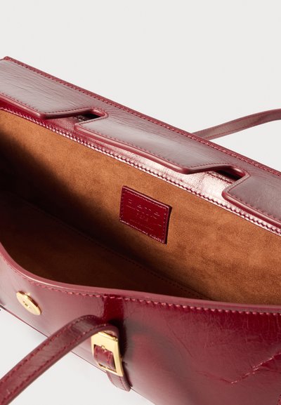 Μπορντό δερμάτινη τσάντα χειρός με λεία, γυαλιστερή επιφάνεια. Διαθέτει σουέτ εσωτερικό, διπλούς κορυφαίους χειρολισθήρες και μικρές χρυσές λεπτομέρειες.