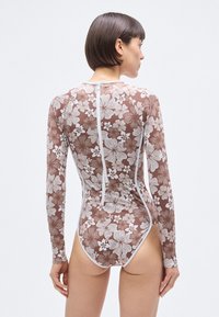 Long-sleeve swimsuit in brown with a floral white pattern. Features a high collar and a back zipper for closure. Made of stretchy material.