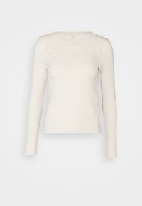 Långärmad, figursydd, krämfärgad stickad topp med rund halsringning och dekorativa perforerade mönster på bröstet och axlarna.