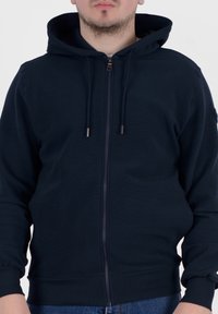 Felpa con zip di colore blu navy realizzata in tessuto morbido, con cappuccio foderato, cordini e polsini a coste, dal taglio comodo e con tasche frontali.