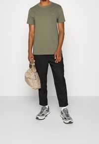 Olive green short-sleeve t-shirt, black pants, grey and white athletic sneakers, and a beige crossbody bag with a textured finish.