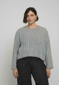 Pullover grigio a coste con scollatura a girocollo, maniche lunghe e orlo corto, abbinato a pantaloni neri testurizzati.