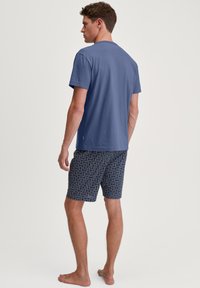 Blauwe katoenen T-shirt voor mannen gecombineerd met gestreepte marineblauwe shorts met een wervelend ontwerp. De stof lijkt zacht en lichtgewicht.