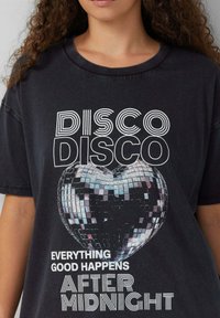 Czarna koszulka graficzna z sercowym dyskotekowym balonem i napisem "DISCO DISCO WSZYSTKO DOBRE DZIEJE SIĘ PO PÓŁNOCY" na białym tle.