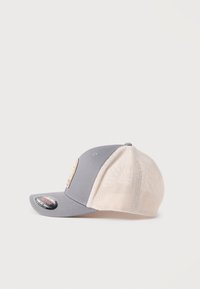 Γκρίζο και μπεζ καπέλο τύπου trucker με δίχτυ, επίπεδη γείσα και επωνυμη πινακίδα στο μπροστινό μέρος, απεικονίζεται από το πλάι σε λευκό φόντο.