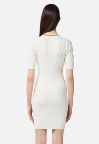 Weißes, gestricktes Kleid mit einem strukturierten Diamantmuster, kurzen Ärmeln und einer taillierten Silhouette. Besitzt einen gerippten Saum und einen Halsausschnitt.