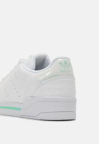 Tenisky Adidas Court Tourino v bílé kůži s mátovými akcenty; perforované boční detaily a texturovaná gumová podrážka, s logem na patě.
