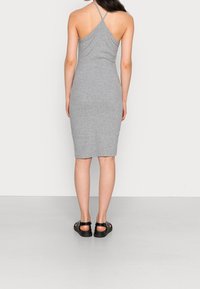 Szara sukienka bodycon z halterneck, charakteryzująca się dopasowanym krojem i długością do kolan. Noszona z czarnymi sandałami na neutralnym tle.