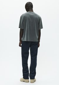 Szary bawełniany t-shirt o luźnym kroju, krótki rękaw, zaokrąglony dekolt, w zestawie z granatowymi spodniami i beżowym obuwiem.