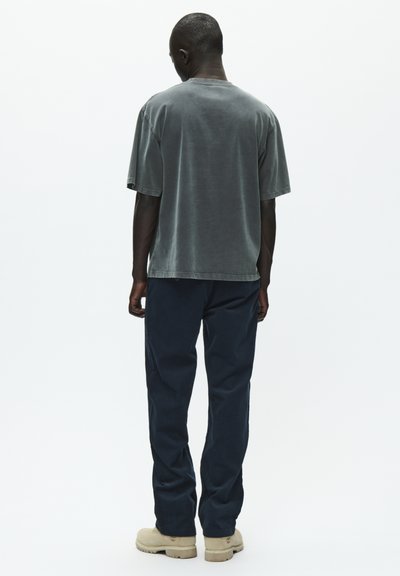 T-shirt in cotone grigio con una vestibilità rilassata, maniche corte e scollatura rotonda, abbinato a pantaloni blu navy e calzature beige.