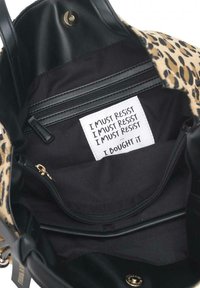 Borsa tote con stampa leopardata e dettagli in pelle nera. L'interno presenta una tasca con zip e un'etichetta bianca con testo stampato, "DEVO RESISTERE".
