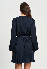 Temno modra obleka z dolgimi, napihnjenimi rokavi, zategnjenim pasom in razširjenim krilom. Narejena iz gladkega, lahkega materiala z večplastno zasnovo.