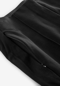 Mustaa kangasta, jossa on teksturoitu pinta, ja sivussa on vetoketjullinen tasku. Materiaali näyttää sileältä ja rakenteellisesti kestävältä.