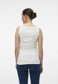 Vit ärmlös topp med rund halsringning, åtsittande design och slät bomullstextur, matchad med mörkblå jeans med bakfickor.