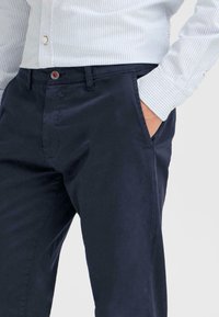 Navyblå chinos med en jevn tekstur, med sidelommer og knappelukking. Kombinert med en lys stripete skjorte.