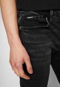 Jeans in denim nero con vestibilità slim. Le caratteristiche includono tasche frontali, una leggera scoloritura e un'etichetta del marchio sulla tasca frontale. Tessuto testurizzato.