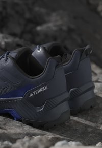 Paire de chaussures de randonnée Adidas Terrex bleu foncé reposant sur une surface rocheuse avec des semelles texturées et robustes visibles.