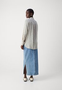 Long-sleeve patterned blouse with diamond design, beige and teal colors, paired with a high-waisted denim skirt featuring a side slit.