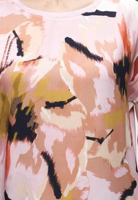 Κοντινό πλάνο ροζ παστέλ μπλούζας με αφηρημένα σχέδια από πινελιές σε μαύρο, μπεζ, μουσταρδί και ανοιχτό κοραλλί.