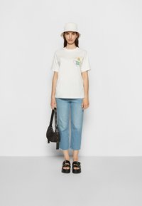 T-shirt branca de algodão com gráfico espiral colorido, jeans cropped azul claro, mala preta e sandálias de plataforma com detalhe de fivela.