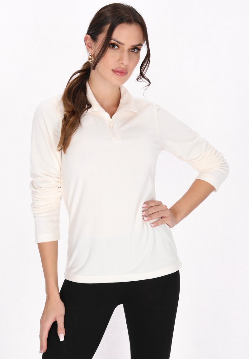 Lyscremet pullover med zipkrave, lange ærmer og blød tekstur, parret med sorte leggings.