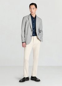 Hellgrauer maßgeschneiderter Blazer, dunkelblaues Hemd mit Knopfleiste, cremefarbene Hose und schwarze Schuhe. Der Blazer verfügt über zwei Taschen und eine klassische Passform.