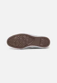 Semelle de chaussure en caoutchouc brun avec un motif de relief en losanges, bordure blanche et logo de la marque en relief. Texture lisse avec des accents en grille.