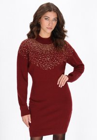 Burgunderfarbenes Strickkleid mit langen Ärmeln, das ein strukturiertes Perlenmuster am Ausschnitt und eine figurbetonte Silhouette aufweist.