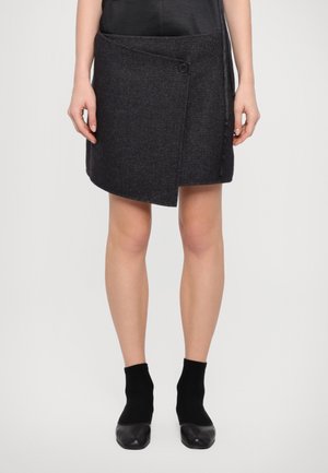 Grey wrap skirt made of textured fabric, featuring a side button closure, asymmetrical hem, and paired with black ankle socks and shoes.