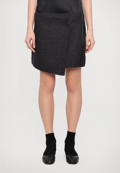 Jupe-culotte grise en tissu texturé, dotée d'une fermeture à bouton sur le côté, d'un ourlet asymétrique, et accompagnée de chaussettes noires et de chaussures.