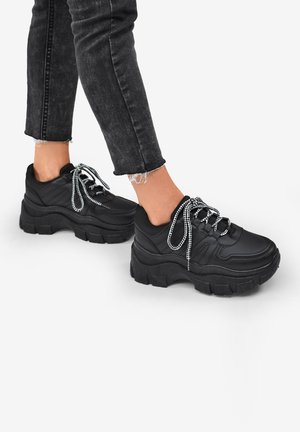 Black chunky sneakers made of smooth material, featuring thick soles, contrasting lace, and a streamlined design with padded accents.