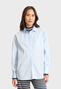 Camicia azzurra chiara in un taglio rilassato con taschino sul petto, realizzata in tessuto di cotone. Maniche lunghe e design colletto classico.
