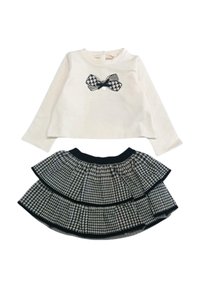 Maglietta bianca a maniche lunghe con grafica di un fiocco nero, abbinata a una gonna a strati con motivo houndstooth bianco e nero e vita elasticizzata.