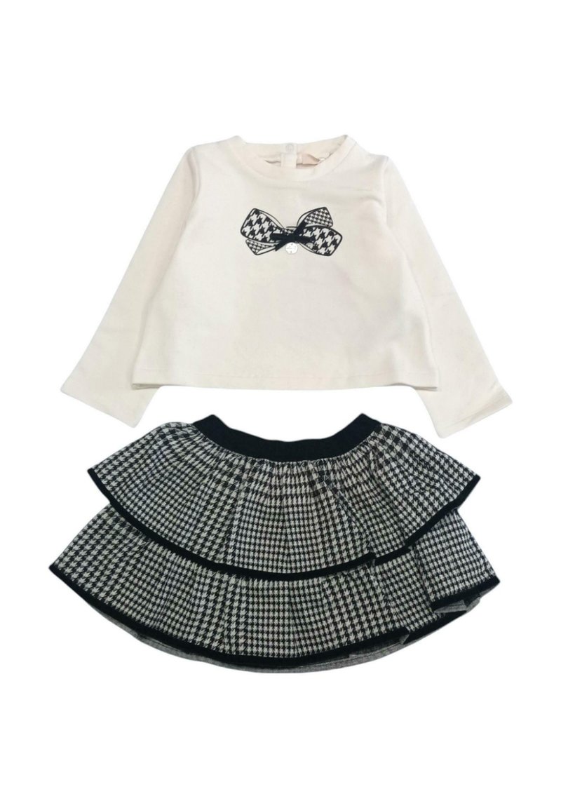 Maglietta bianca a maniche lunghe con grafica di un fiocco nero, abbinata a una gonna a strati con motivo houndstooth bianco e nero e vita elasticizzata.