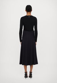 Musta pitkähihainen toppi, jossa on pieni logo takana, yhdistetty tumman violetin midi-hameen kanssa. Asusteessa on sileä pinta ja muotoiltu siluetti.