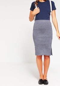 Marineblå t-shirt med axelremmar, matchad med en åtsittande grå pennkjol med en sidssprund och texturerad tyg. Svarta loafers. 