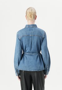 Denimshirt met een ceintuur in de taille, lange mouwen en een rugplooival. Voorzien van een klassieke kraag en knoopmanchetten in een lichtblauwe tint.